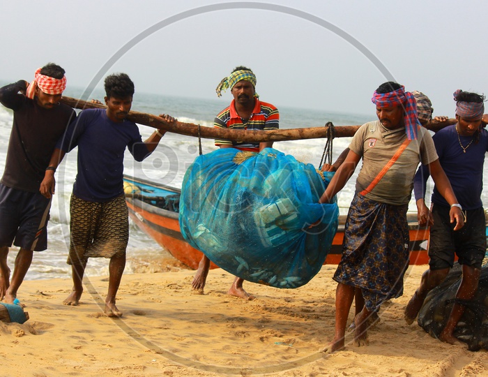 Fishermen spreading out freshly caught fish to dry on blue net in the beach
