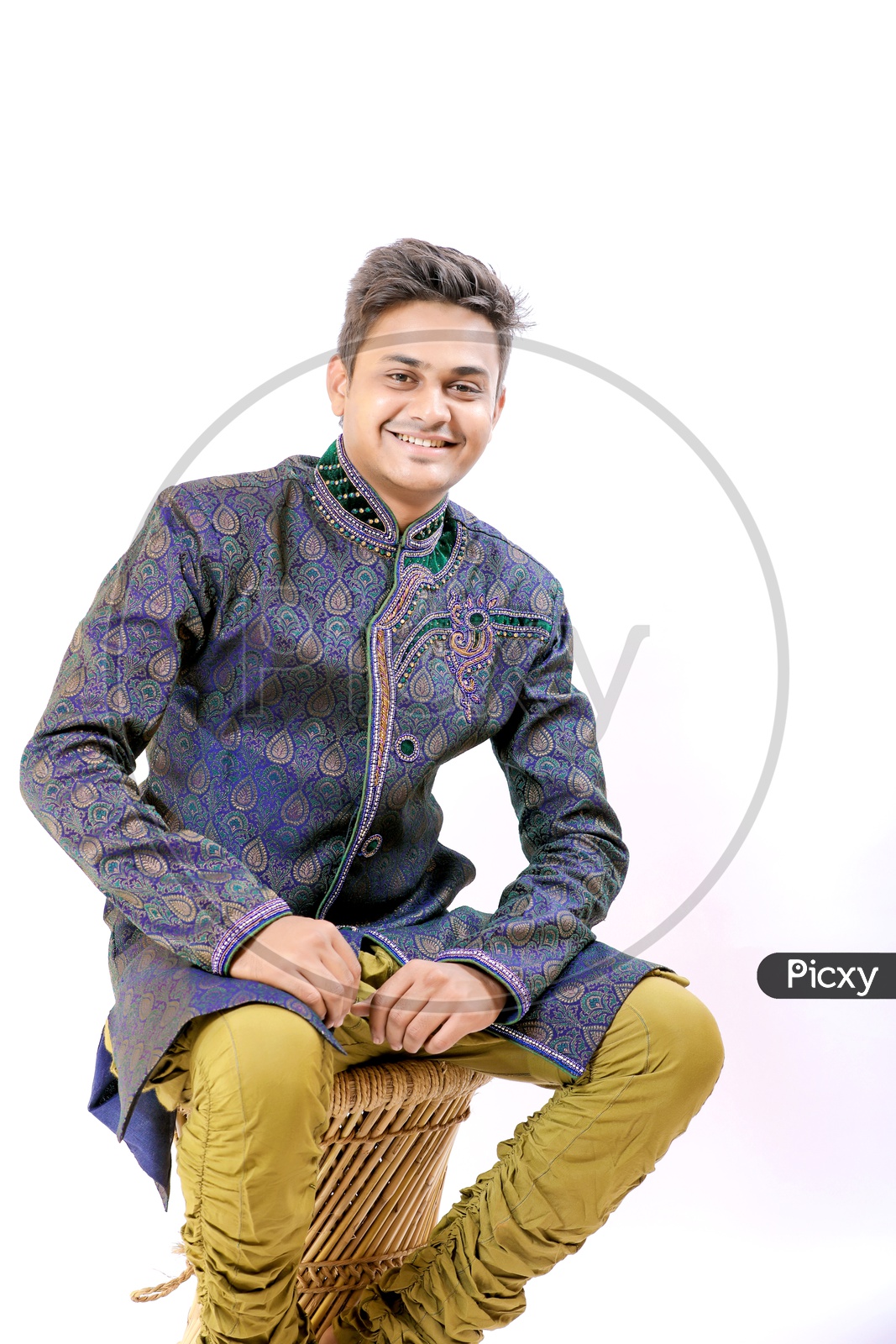 A Confident young Indian Man Sitting in a Chair with a Smiling Face looking to Camera On an Isolated White Background