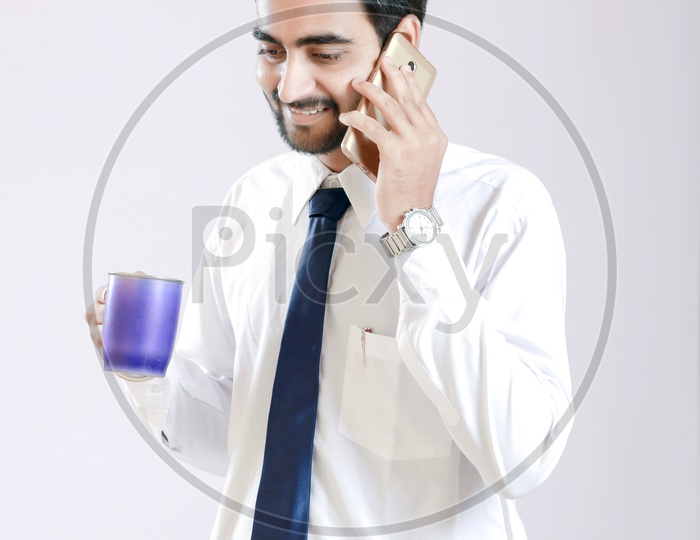 Young Indian Man talking on Smartphone and Holding Cup in Hand