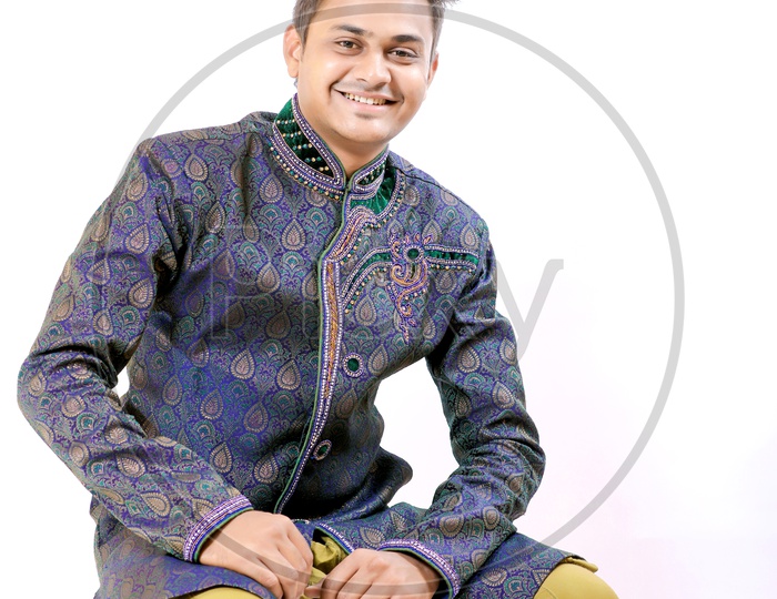 A Confident young Indian Man Sitting in a Chair with a Smiling Face looking to Camera On an Isolated White Background
