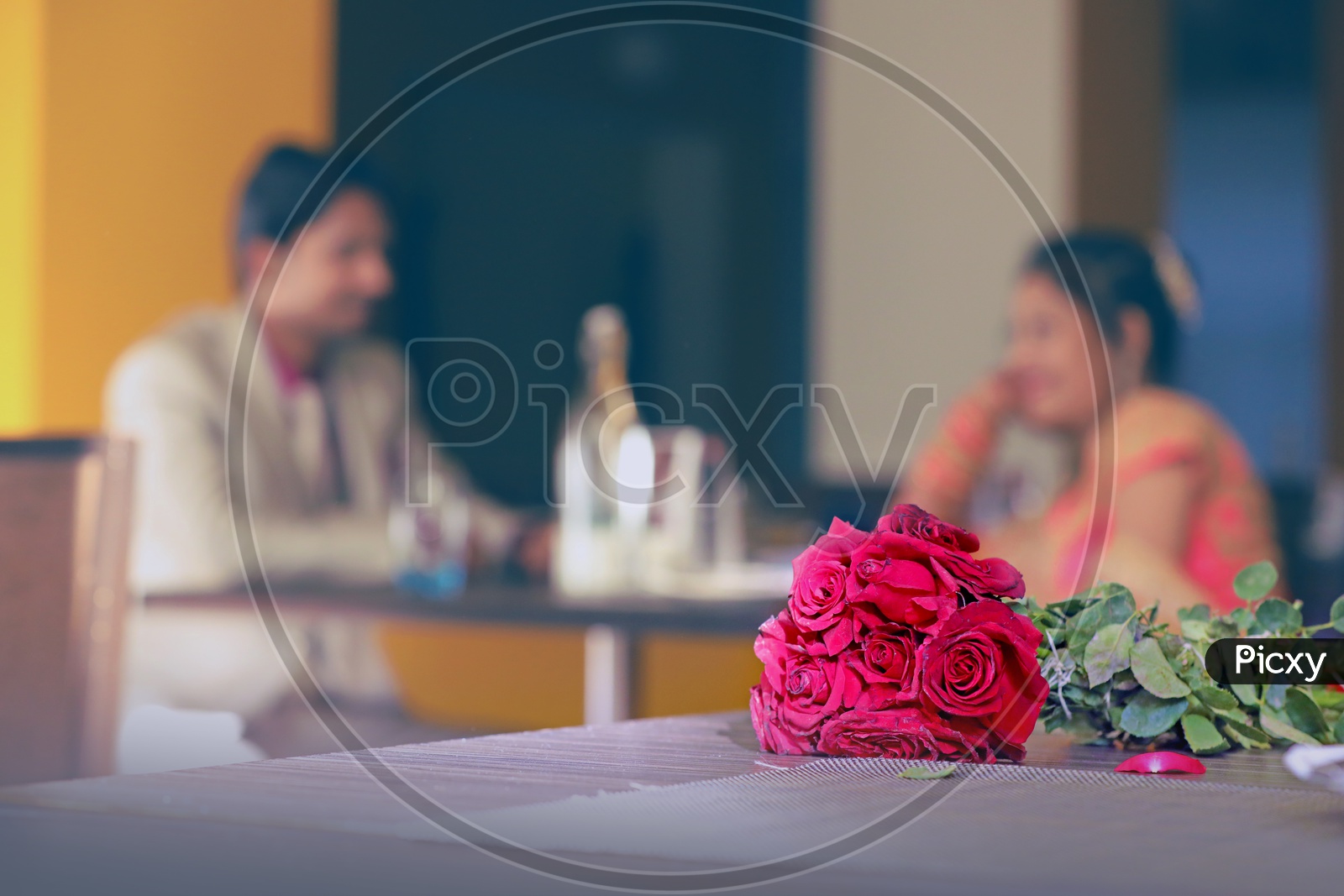 Bride and Grrom Sitting in a Restaurant with a Red Rose Bouquet in Focus