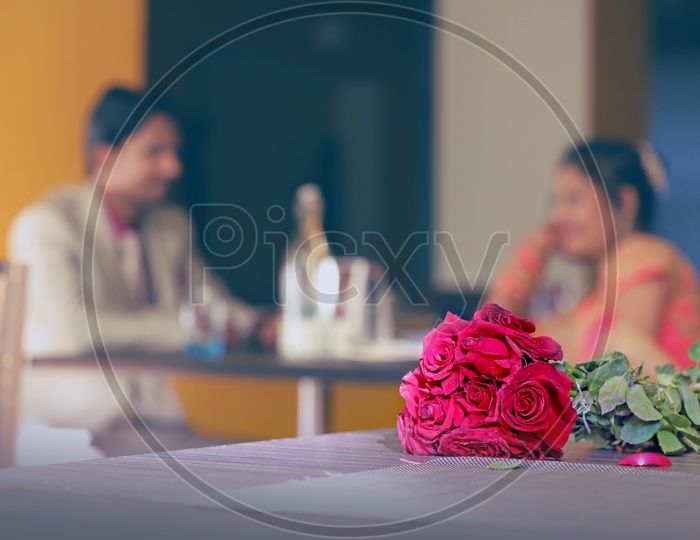 Bride and Grrom Sitting in a Restaurant with a Red Rose Bouquet in Focus