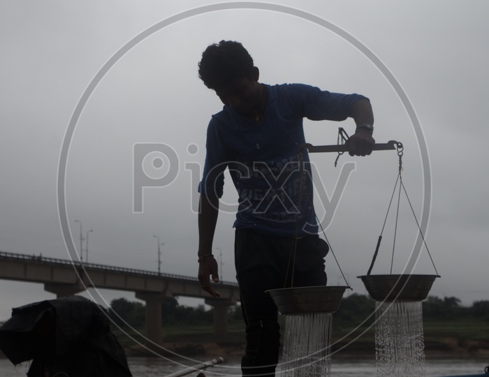 A Man weighing fishes on the bank of Godavari.
