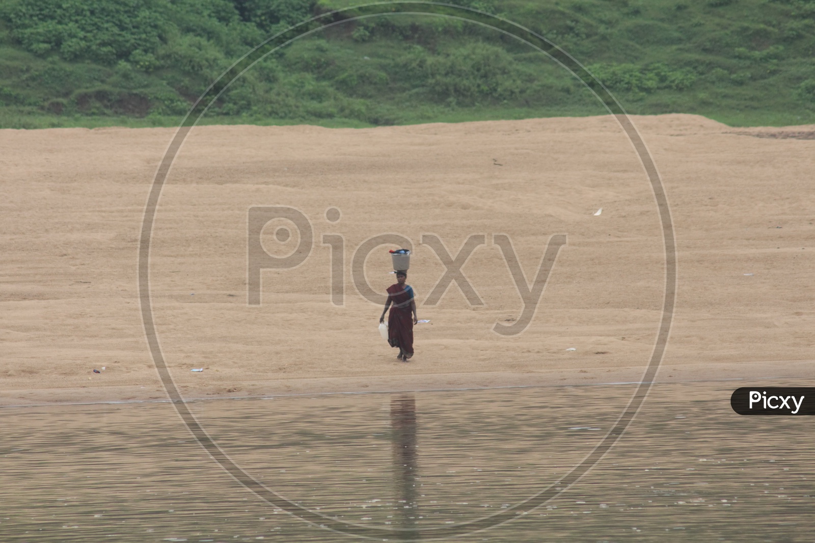 A woman walking on the bank of river godavari with bucket on her head.