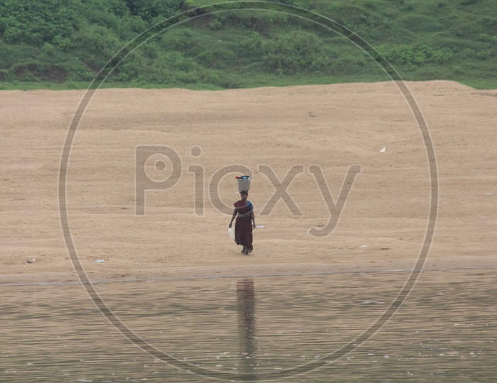 A woman walking on the bank of river godavari with bucket on her head.
