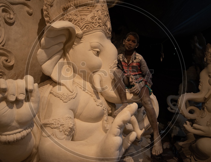 A Boy Child Sitting on a Ganesh idol made Of Plaster of paris
