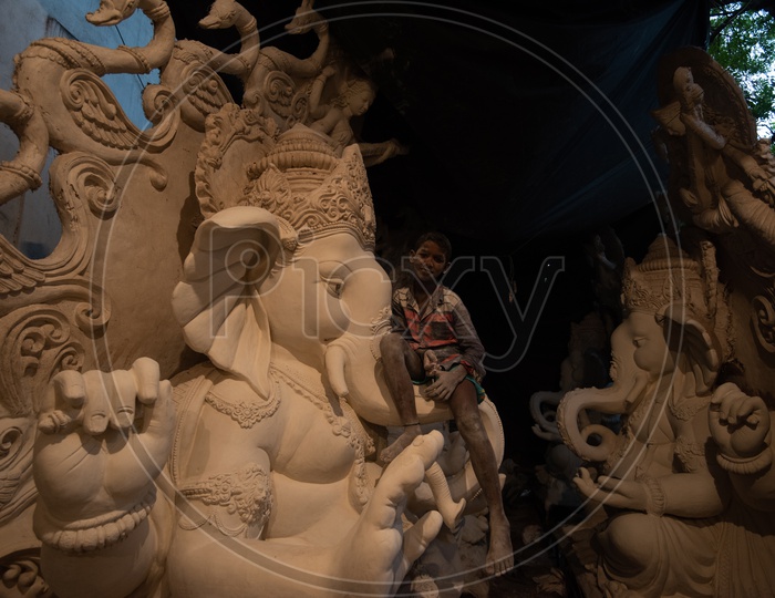A Boy Child Sitting on a Ganesh idol made Of Plaster of paris