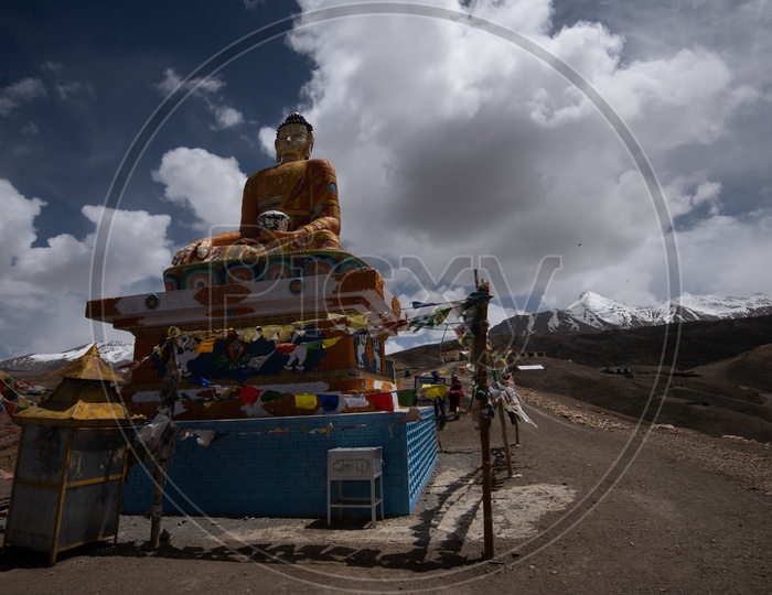 A Buddha Statue  with Colorful tibetan Flags and Mountains and Dunes In Background