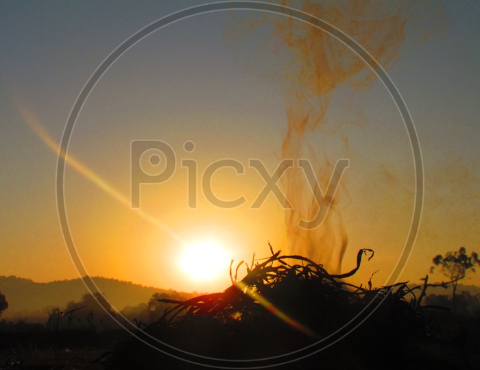 Smoke Coming From a Camp Fire in Agricultural Fields With Sunset In Background