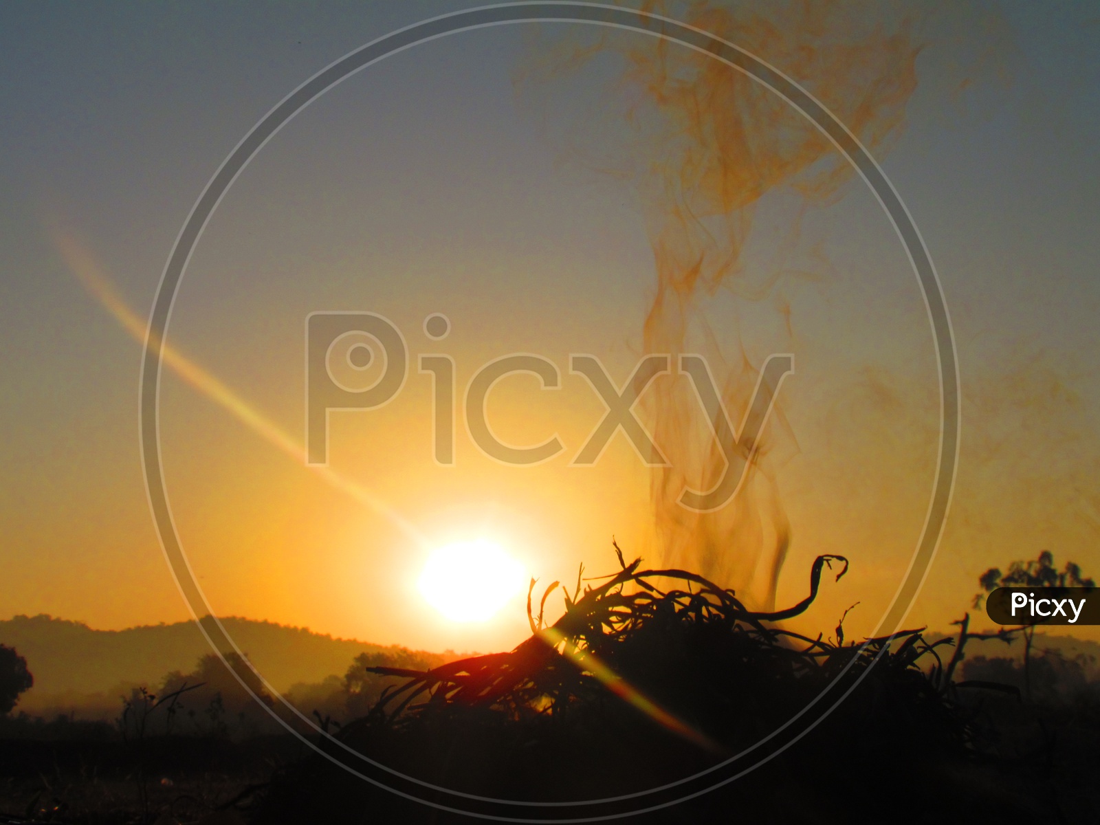 Smoke Coming From a Camp Fire in Agricultural Fields With Sunset In Background
