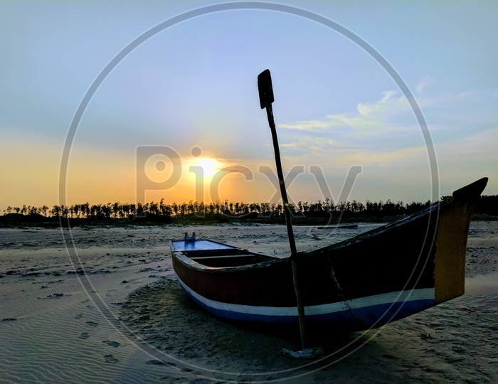A Lone Boat In a Beach With Sand and Sunset In Background