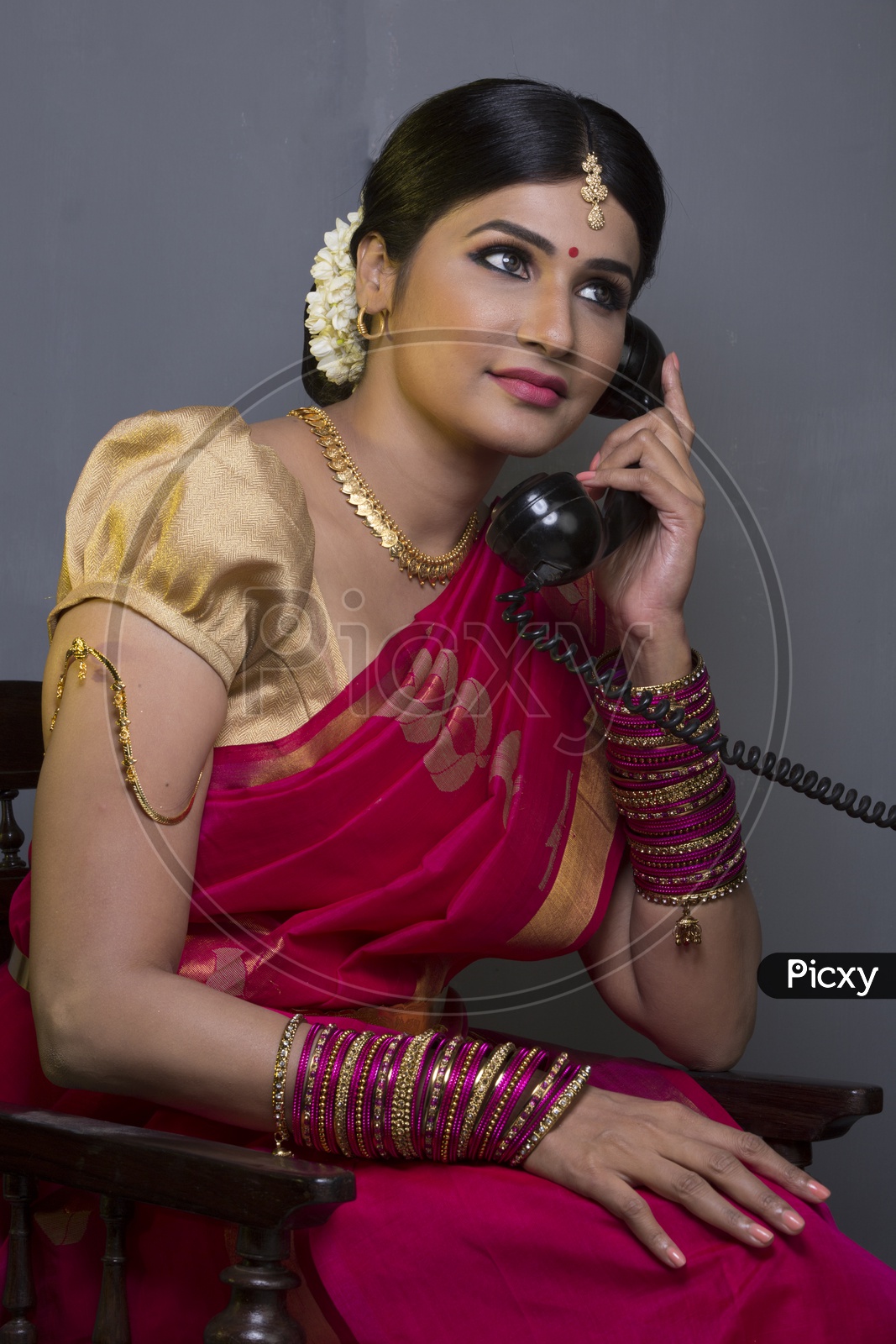 Indian Bride dressed up in red saree talking through a phone portrait in Studio Lighting / Traditionally dressed up girl