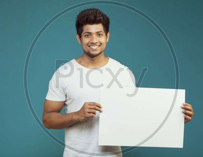 An Indian Male Model Showing an Empty Placard And Looking to Camera and Smiling on an Isolated Background