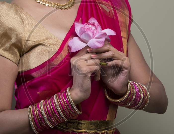 A Beautiful Indian Female Model  in Traditional Attire Wearing a Saree and Jewelry with a Lotus flower in  Hands Closeup Shot  on an Isolated Gery Background