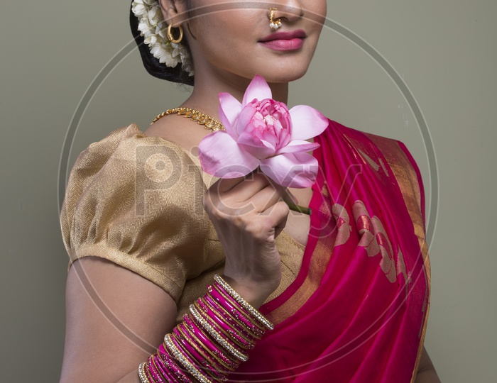 Indian bride dressed up in red saree with flower in hand portrait in Studio Lighting / Traditionally dressed up girl