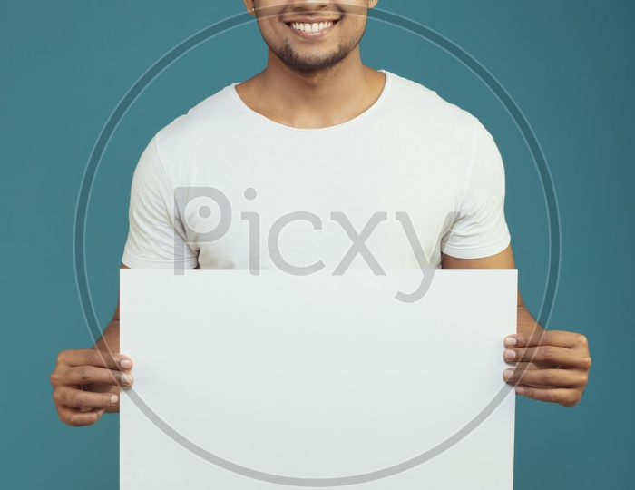 An Indian Male Model Showing an Empty Placard And Looking to Camera and Smiling on an Isolated Background