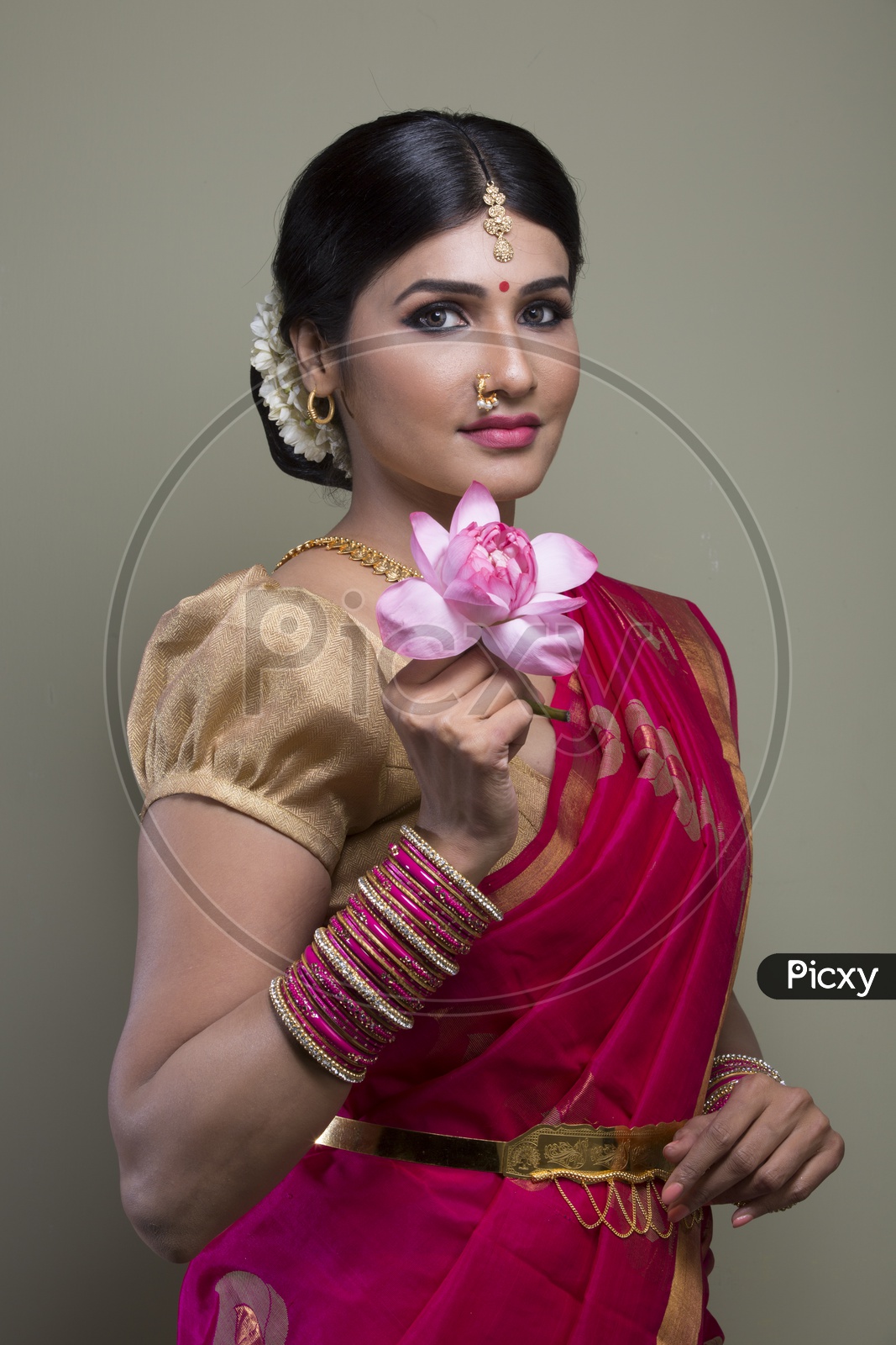 A Beautiful Indian Female Model  in Traditional Attire Wearing a Saree and Jewelry with an Expression and With a Lotus Flower in Hand  on an Studio Closeup shot