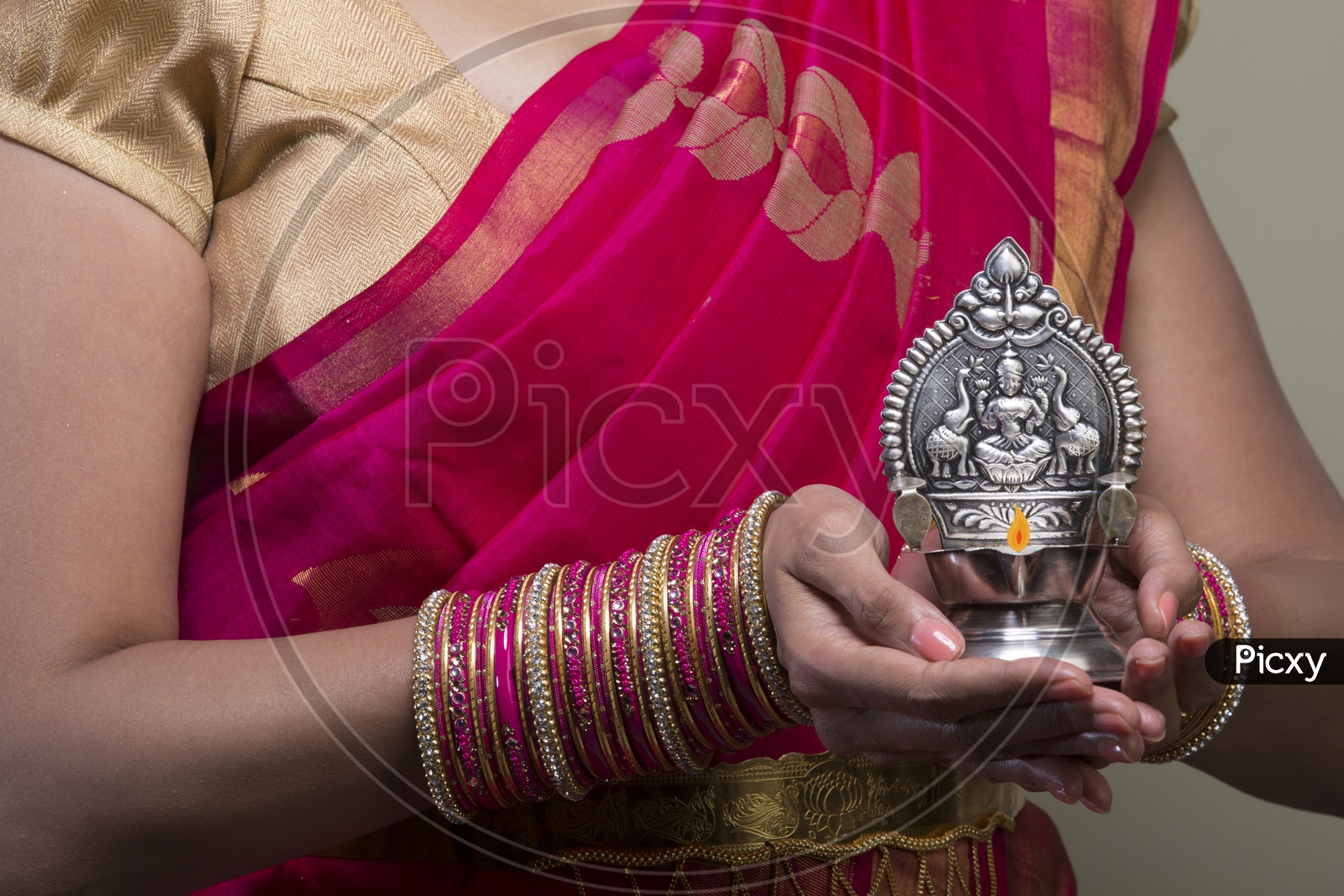 A Beautiful Indian Female Model  in Traditional Attire Wearing a Saree and Jewelry  With a Traditional Silver Oil Lamp In Hands  Closeup Shot