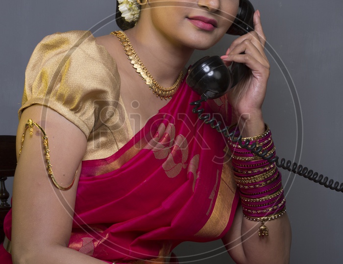 Indian Bride dressed up in red saree talking through a phone portrait in Studio Lighting / Traditionally dressed up girl
