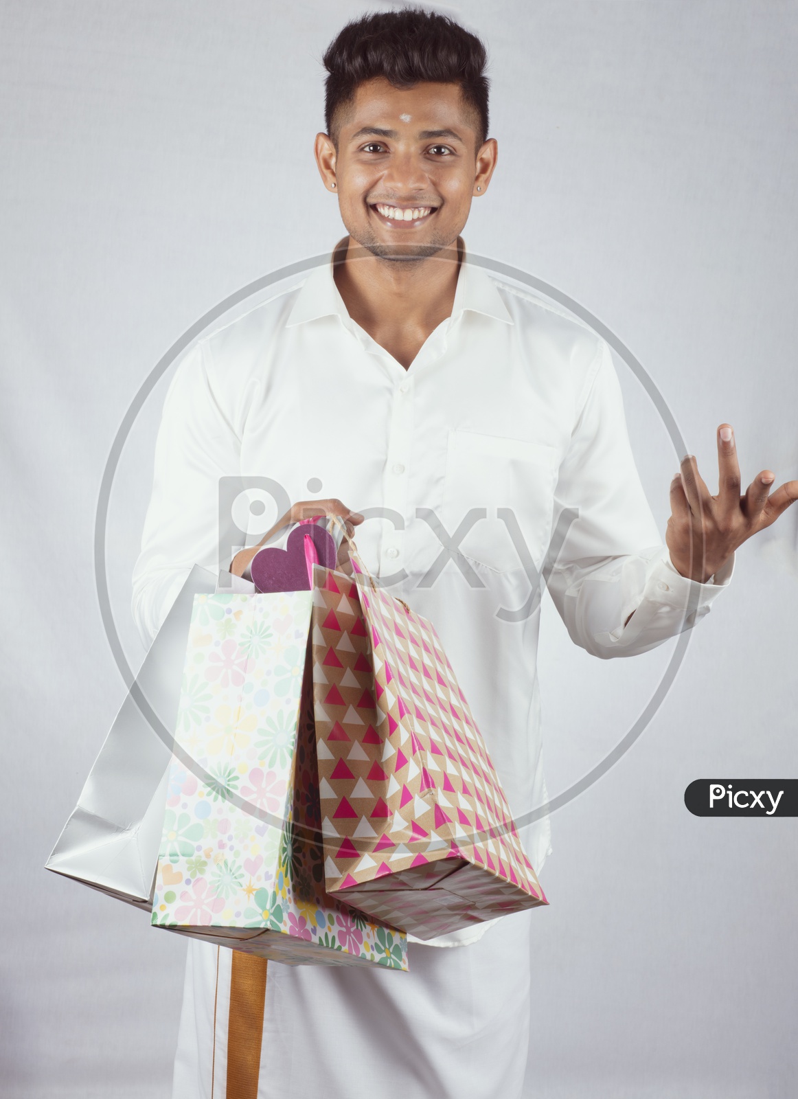 An Indian Male Model In traditional South Indian Attire with Shopping Bags in One Hand and with Smiling Face with expression  on an Isolated White Background