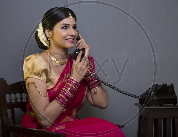 A Beautiful Indian Female Model  in Traditional Attire Wearing a Saree and Jewelry with an Expression and  Speaking in Phone on an Studio Closeup shot