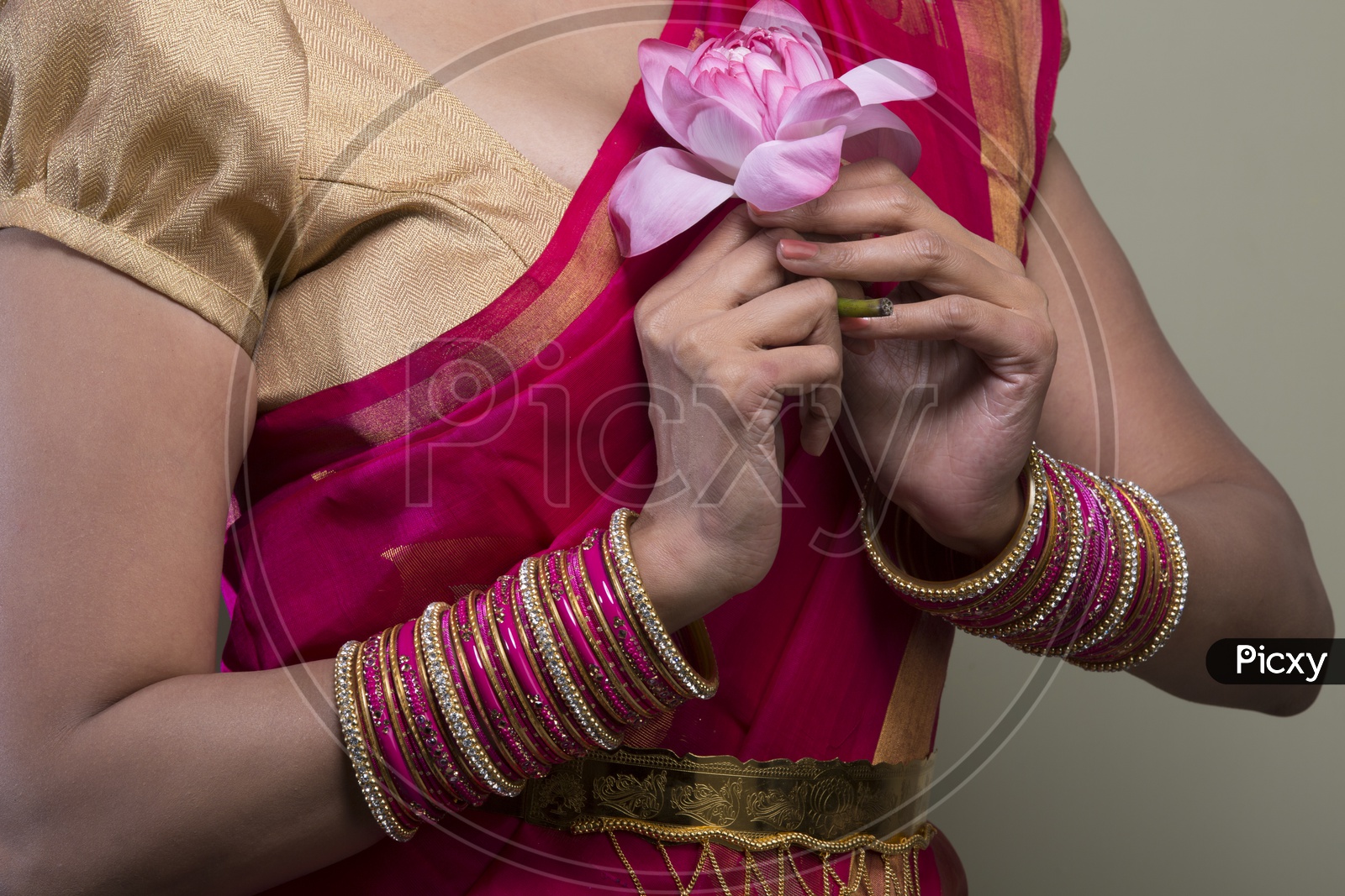 A Beautiful Indian Female Model  in Traditional Attire Wearing a Saree and Jewelry with a Lotus flower in  Hands Closeup Shot  on an Isolated Gery Background