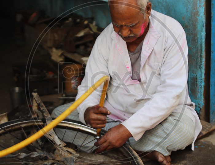 Old man repairing Bicycle tyre with coloured face in Barsana