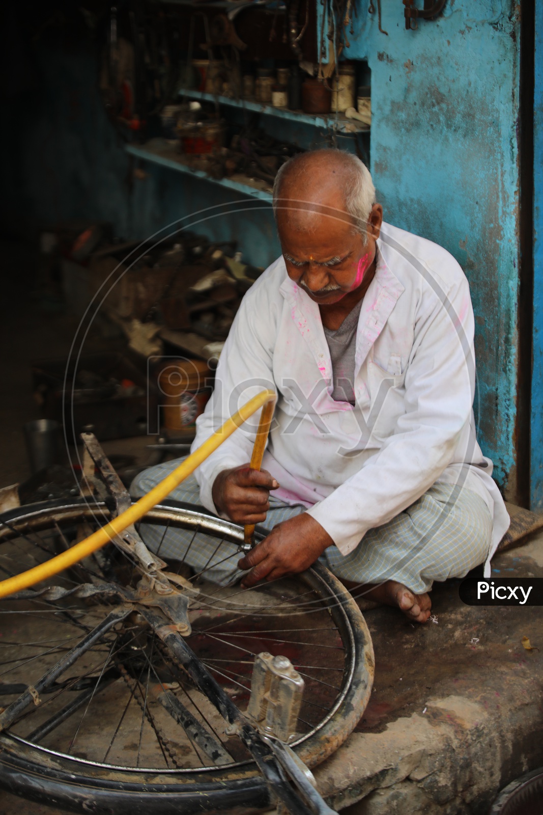 Old man repairing Bicycle tyre with coloured face in Barsana