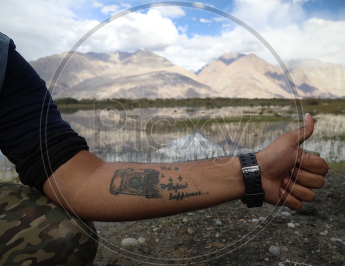 A Photographer With a Camera tattoo on his Hand In River valley of Leh