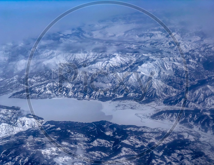 Ariel View of Snow Capped Mountains, Clouds, Blue Sky & Frozen lake