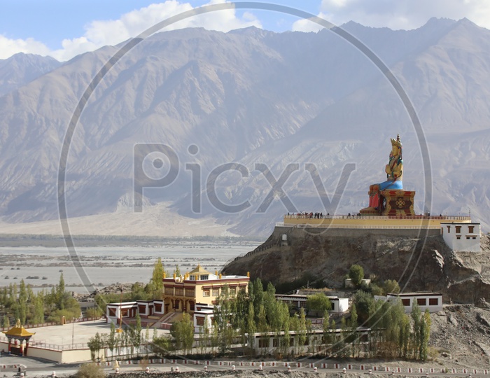 Statue of Buddha in leh with snow capped mountains in the background / Diskit Monastery, Diskit Gompa