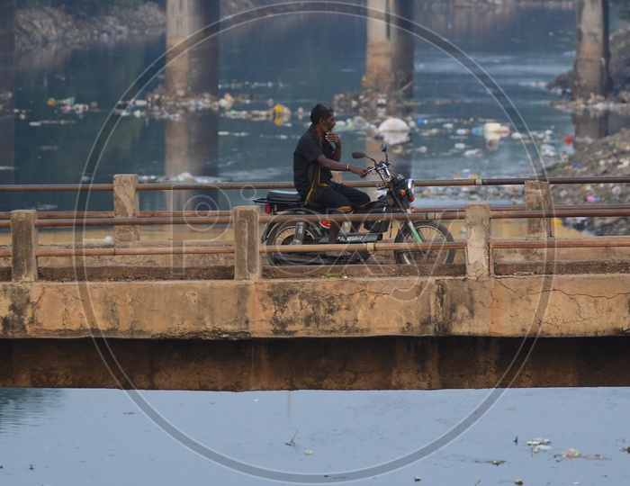 A man rides a motor cycle on a bridge, rivas canal