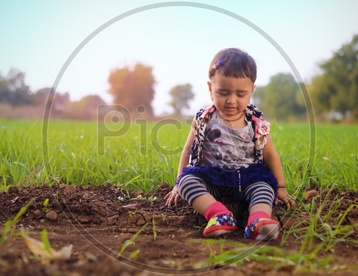 Baby girl is sitting in the middle of the agriculture fields