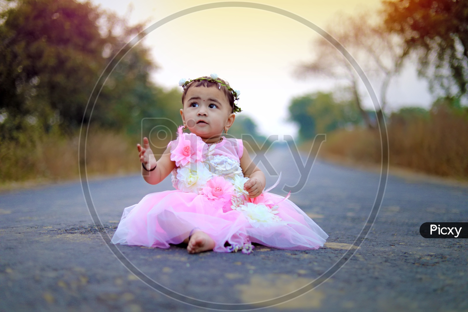 Baby girl with a flower hair band sitting in the middle of the road