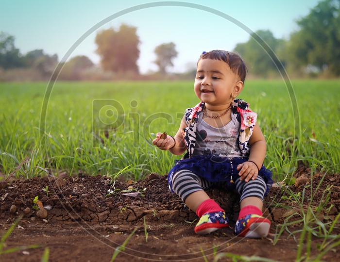 Baby girl is sitting in the middle of the agriculture fields and Playing with mud