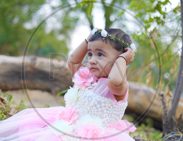Baby girl in Pink frock sitting in the middle of the fields - playing with a flower hair band