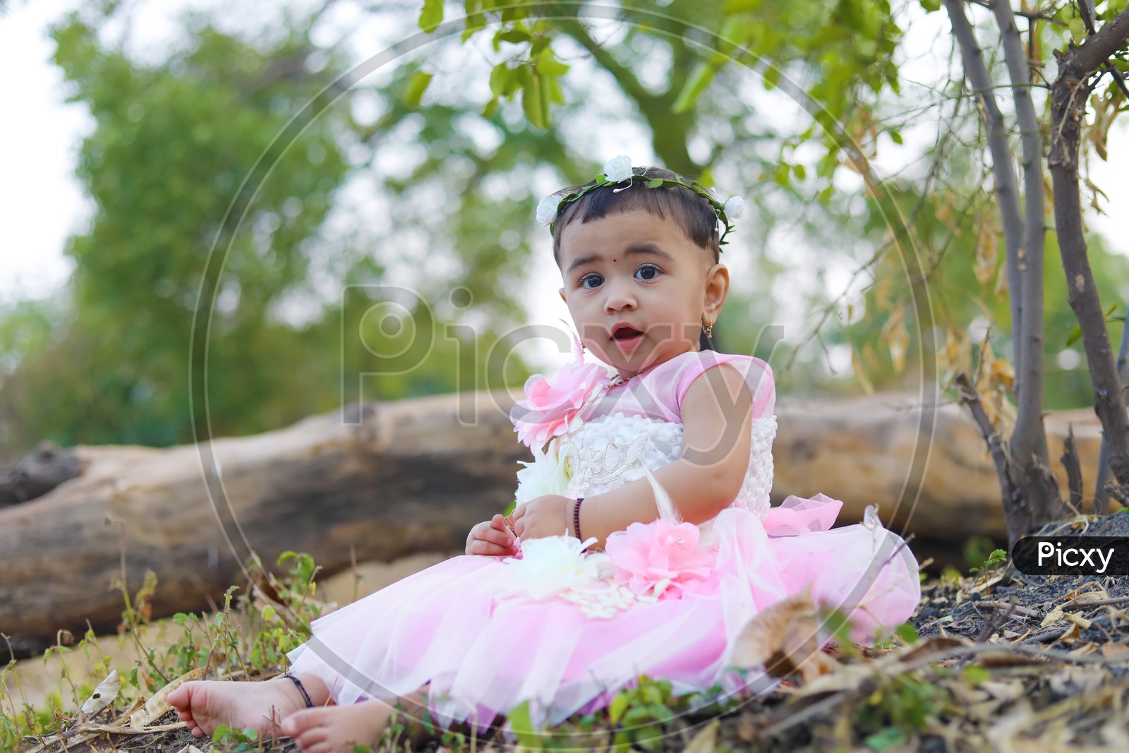 Baby girl in Pink frock with a flower hair band sitting in the middle of the fields