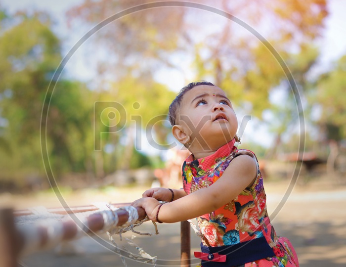 Baby girl playing with a flower near a cot