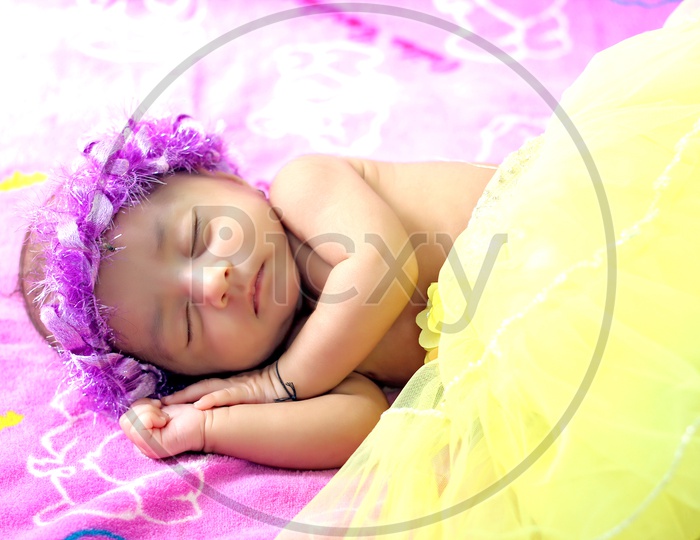 Cute new born baby girl with flower hair band lying down on the bed