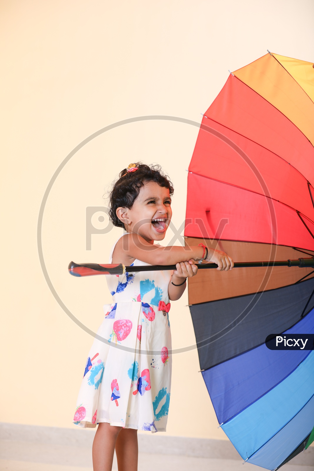 Indian girl dressed in colorful frock playing  with rainbow colored umbrella