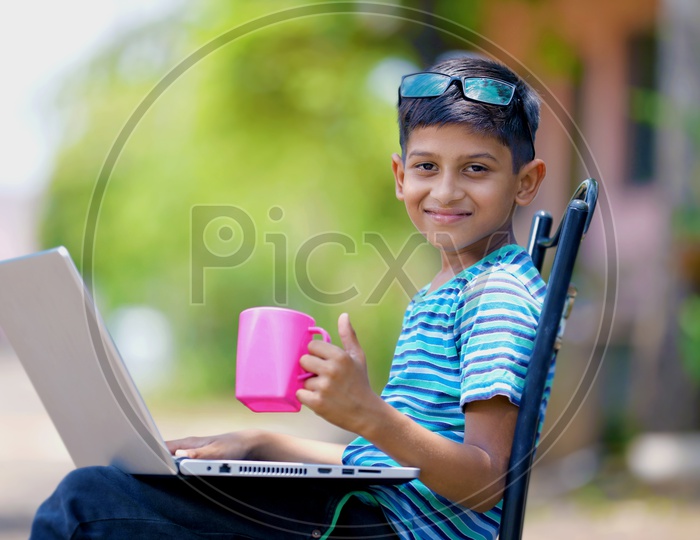 Indian Child holding Cup in Hand and using Laptop