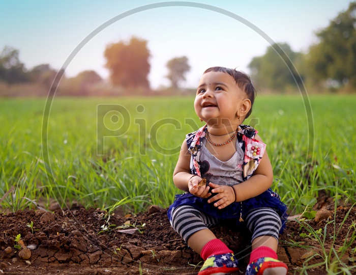 Baby girl is sitting in the middle of the agriculture fields and laughing