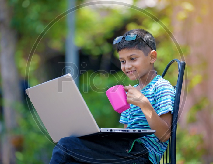 Indian Child holding Cup in Hand and using Laptop
