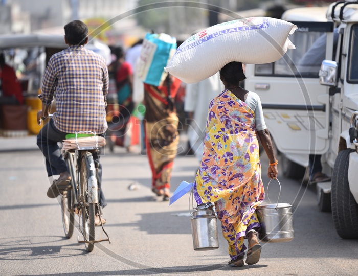 A Woman Carrying Heavy Weight on her Head and Steel Carriers in Hand Walking Along a Road As a Part Of her Daily Routine