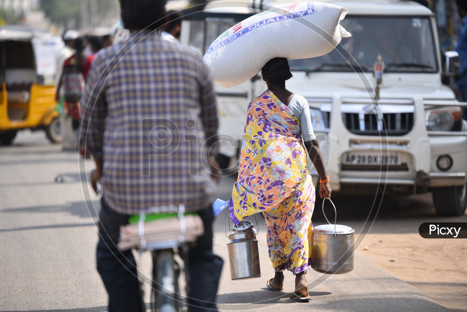 A Woman Carrying Heavy Weight on her Head and Steel Carriers in Hand Walking Along a Road As a Part Of her Daily Routine