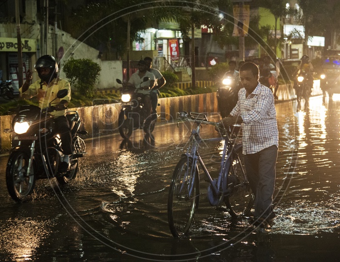 A man crosses a waterlogged road with a bicycle  in Vijayawada after a heavy rain on 03/05/18
