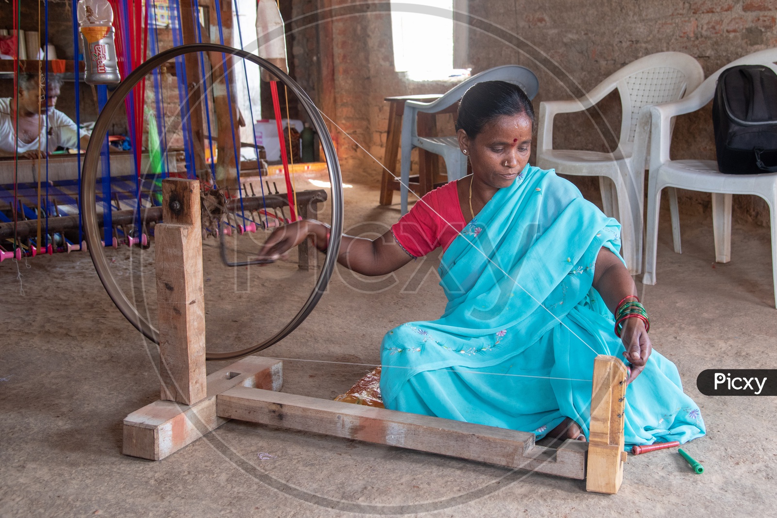 Women working on hand operated spinning wheel for weaving