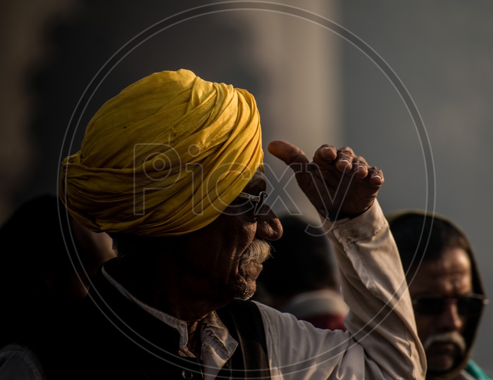 An old man with turban covering his face in harsh sun