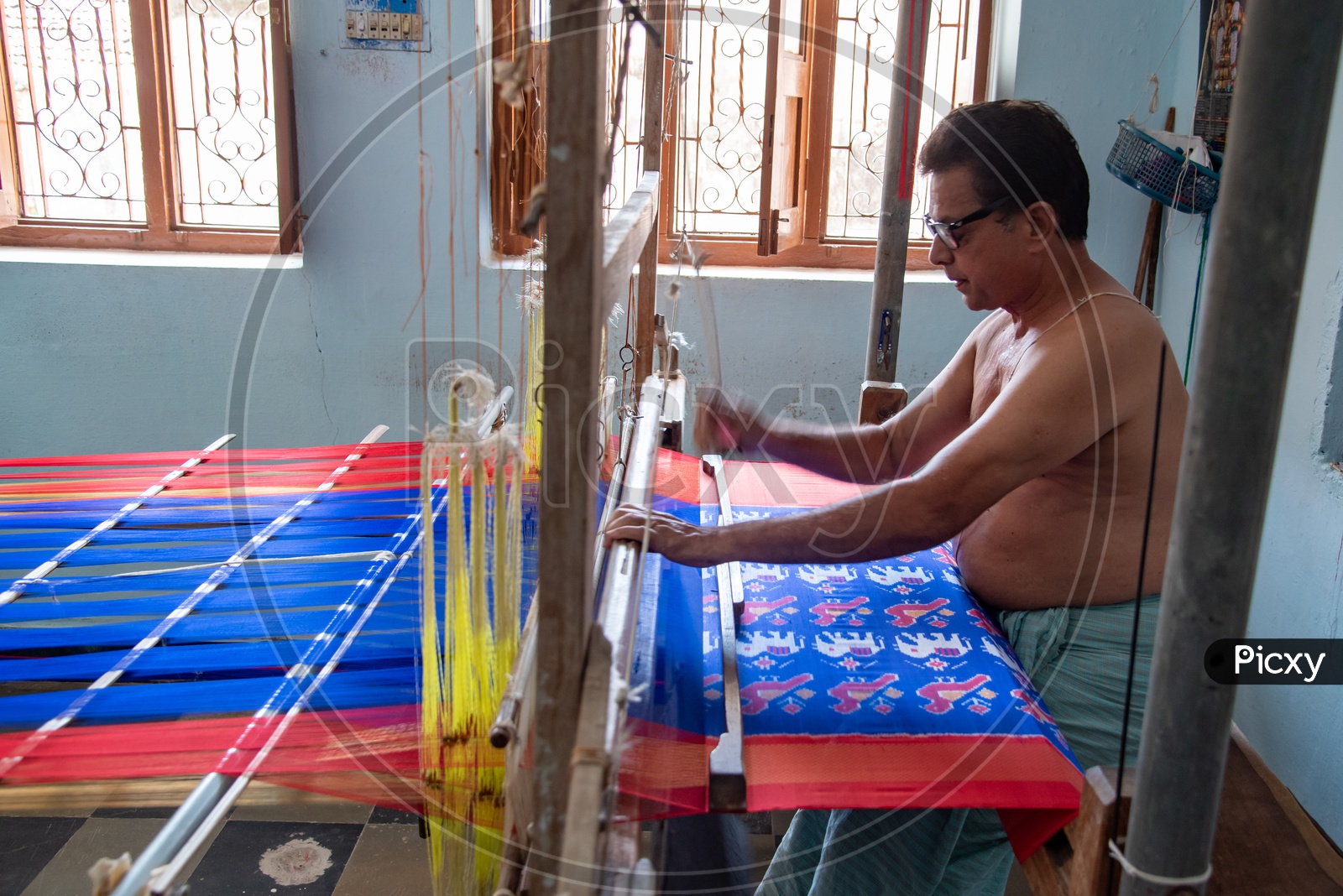 Artisan weaver working on hand operated spindle weaving machine to make sarees