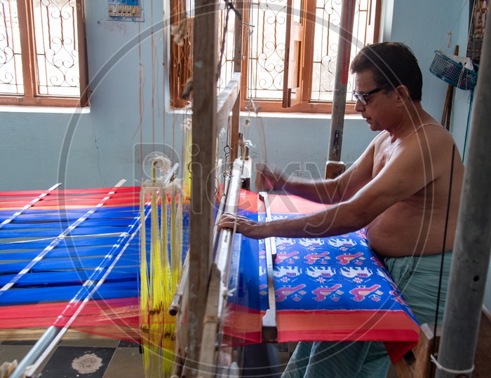 Artisan weaver working on hand operated spindle weaving machine to make sarees